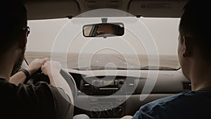 View inside car. Two man traveling by car through country road. Male in sunglasses driving car and talking with friend.