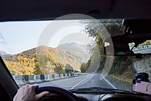 View from inside car window to the road and autumn mountain landscape. Asphalt road in perspective in a sunny day