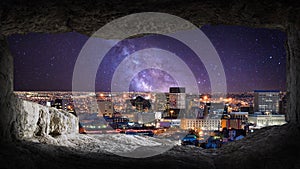 View from the inside of the cave to the night panorama of the city, milky way in the background