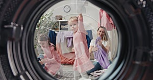 A view from inside the drum of a young woman and her daughters having fun doing housework, throwing more clothes into