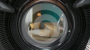 View from inside the empty washing machine with an opened door into the beautiful living room. Slow motion