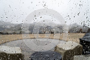 View from inside a hilltop home of a patio and subdivision below as rain falls. Taken through a rain spotted window.