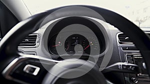 View inside of a passenger car with a dashboard behind a steering wheel. Action. Close up of engine speed scales