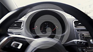 View inside of a passenger car with a dashboard behind a steering wheel. Action. Close up of engine speed scales