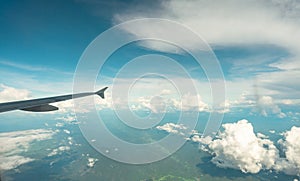 View from inside plane through plane window over blue sky, white clouds and green mountain. Commercial airline flight for summer