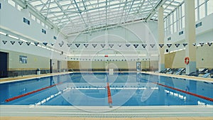 View inside of a swimming pool at the sports complex. Video. Beautiful swimming pool with glass ceiling and calm water.