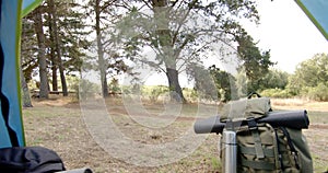 View from inside a tent captures a peaceful forest scene with camping gear in the foreground, with c