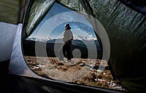 View from inside a tent on the male tourist in his camping in the mountains at night