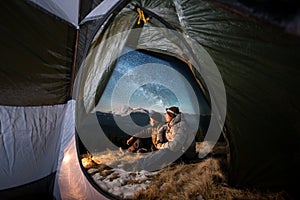 Two male tourists have a rest in the camping in the mountains at night under night sky full of stars and milky way