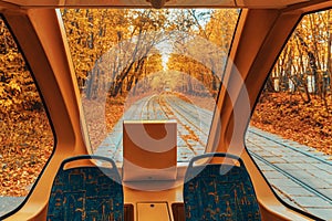 View from from inside of tram window to autumn landscape of park, suburban forest with golden foliage