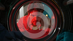 View from inside the washing machine, adult man looking angry inside the washer drum in red light