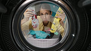 View from inside the washing machine, adult woman looking confused holding a different socks