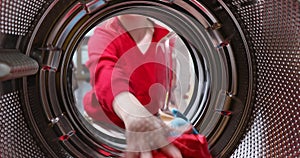 View from inside the washing machine drum, a young woman loading dirty laundry from a basket. Taking clothes out of washing