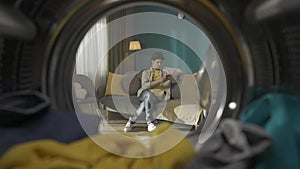 View from inside the washing machine, young man sitting on the couch in the room with smartphone HDR BT2020 HLG Material