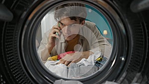 View from inside the washing machine, young man takes out the dirty clothe and talking on smartphone