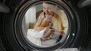 View from inside the washing machine, young woman takes out the dirty clothe and talking on smartphone