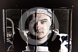 View through iron door with prison bars on young prisoner holding bars in a jail cell