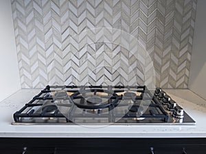 View of an iron stove top with stainless steel knobs inside a kitchen with a nice backsplash