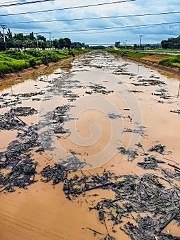 View of irrigation canal with weeds and debris flowing together with strong flowing dirty brown water due to soil and mud from photo