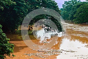 View of irrigation canal with weeds and debris flowing together with strong flowing dirty brown water due to soil and mud from photo