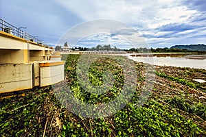 View of irrigation canal with weeds and debris flowing together with strong flowing dirty brown water due to soil and mud from photo