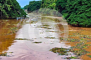 View of irrigation canal with weeds and debris flowing together with strong flowing dirty brown water due to soil and mud from photo