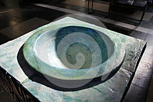 View on isolated green blue old medieval marble stone baptismal font illuminated by natural sunlight in catholic church - Brugge,