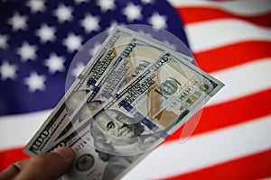 View on isolated hand holding three 100 dollar bank paper notes. Blurred USA flag background. focus on