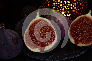 View on isolated raw ripe fig half with group of figs  on black slate stone illuminated by oriental candle lamp