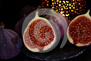 View on isolated raw ripe fig half with group of figs  on black slate stone illuminated by oriental candle lamp