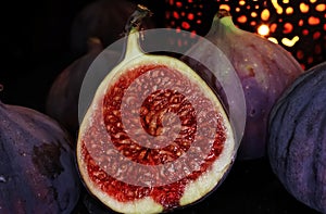 View on isolated raw ripe fig half with group of figs on black slate stone illuminated by oriental candle lamp