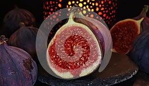 View on isolated raw ripe fig half with group of figs on black slate stone illuminated by oriental candle lamp
