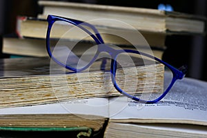 View on isolated stack of old yellowed books on wood table with blue reading glasses and open book