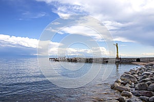 View of Issyk-Kul Lake, a mountain range with snow-capped peaks and a pier from a rocky beach