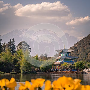 View of the Jade Dragon Snow Mountain and the Black Dragon Pool, Lijiang, Yunnan province, China. The Suocui Bridge with yellow fl