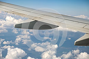 View of jet airplane wing from inside flying over white puffy clouds in blue sky. Travel and air transportation concept