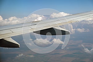 View of jet airplane wing from inside flying over white puffy clouds in blue sky. Travel and air transportation concept