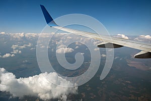 View of jet airplane wing from inside flying over white puffy clouds in blue sky. Travel and air transportation concept