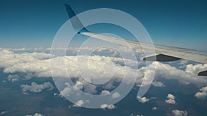 View of jet airplane wing from inside flying over white puffy clouds in blue sky. Travel and air transportation concept