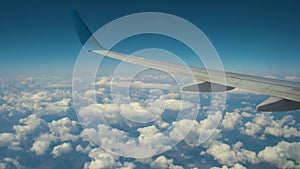 View of jet airplane wing from inside flying over white puffy clouds in blue sky. Travel and air transportation concept