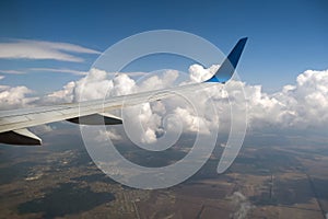 View of jet airplane wing from inside flying over white puffy clouds in blue sky. Travel and air transportation concept