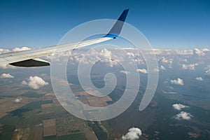 View of jet airplane wing from inside flying over white puffy clouds in blue sky. Travel and air transportation concept