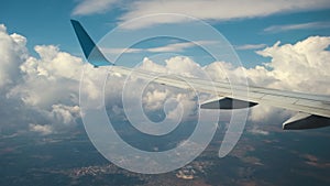 View of jet airplane wing from inside flying through white puffy clouds in blue sky. Travel and air transportation