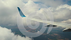 View of jet airplane wing from inside flying through white puffy clouds in blue sky. Travel and air transportation concept.