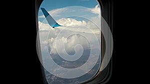 View of jet airplane wing from inside flying through white puffy clouds in blue sky. Travel and air transportation concept.