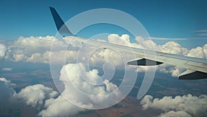 View of jet airplane wing from inside flying through white puffy clouds in blue sky. Travel and air transportation concept.