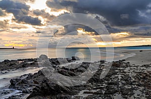 View of La Pelosa beach in Sardinia at sunrise with rocky reef in the foreground