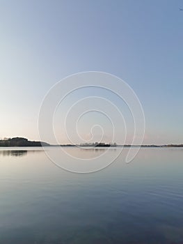View of the lake at dusk. Calm blue water, horizon and clear sky. Tranquility scene of nature. Space for text.