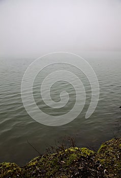 View of a lake on foggy day with the water lapping by the shore