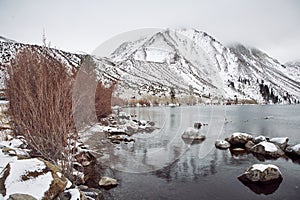 View of Lake on the Mountains in Winter Fog with Dramatic Snow Capped Mountains in the Background